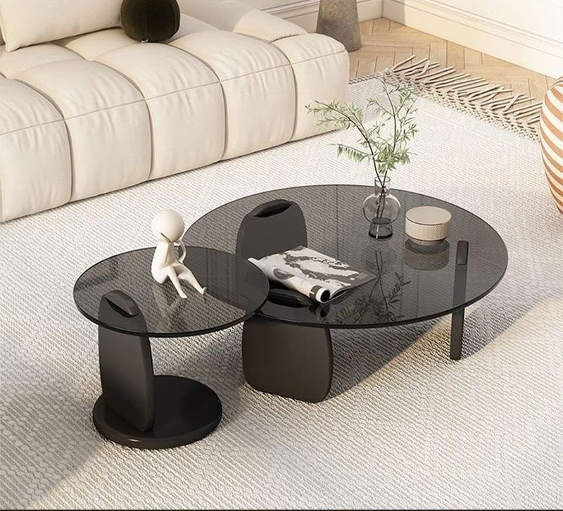 Modern round coffee table and side table set featuring smoked tempered glass tops and sculptural black solid wood bases in a contemporary luxury design.